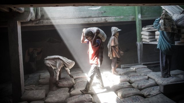 Indonesian porter carries a sack of cement to load on a traditional wooden ship.