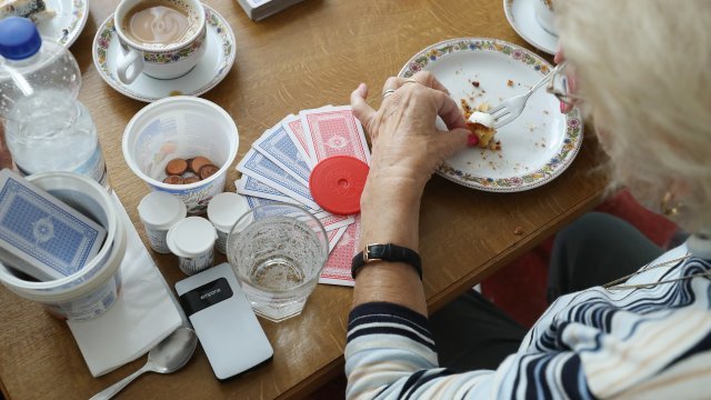 An elderly women finishes eating a piece of cake while taking a break during a card game.