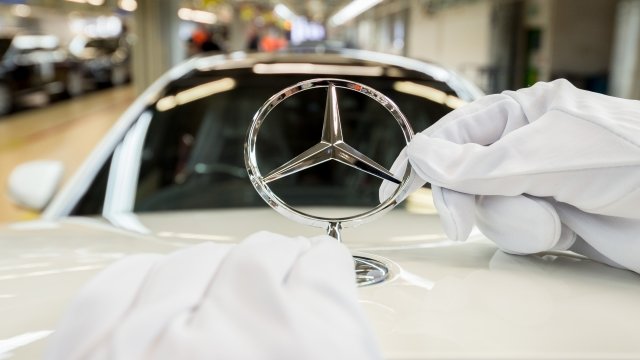 An employee mounts a Mercedes-Benz emblem to the hood of a sedan