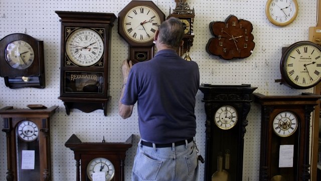 A man stands in front of a wall of clocks