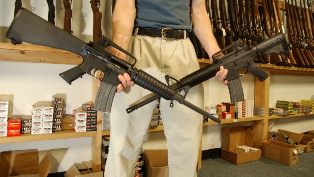 A man holds two Colt AR-15's.