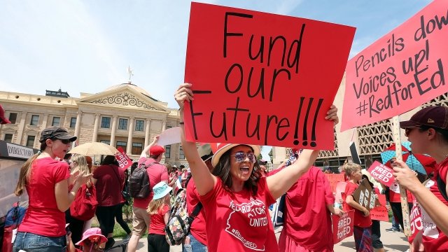 An Arizona teacher holds up a sign in front of the State Capitol.