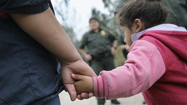 Migrant child with parent with ICE agent in the background