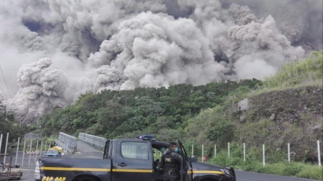 Guatemalan police officer stands in front of a cloud of ash shooting out from the Fuego volcano