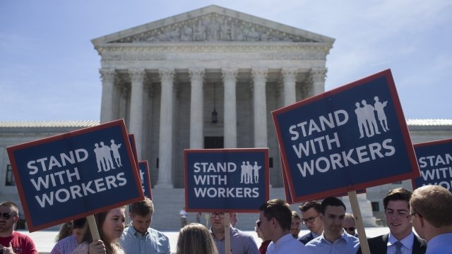People stand outside the U.S. Supreme Court with "Stand with Workers" signs