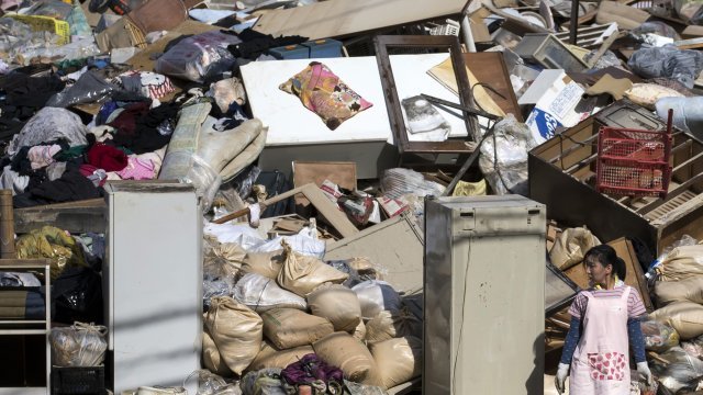Woman stands by pile of items ruined by flooding