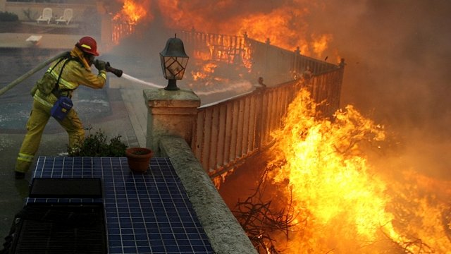 A firefighter attacks wildfire flames near a home.