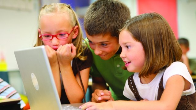 Children look over a computer.