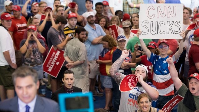A man holds a "CNN Sucks" sign behind reporter Jim Acosta