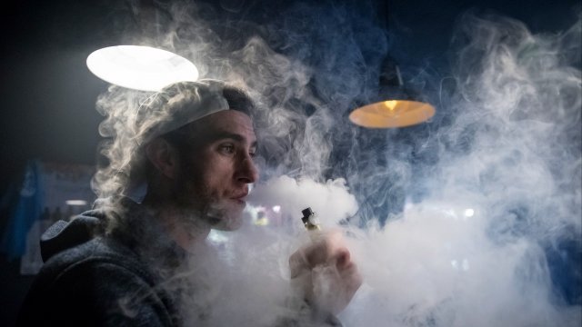 A man who working at a smoke shop exhales vapor