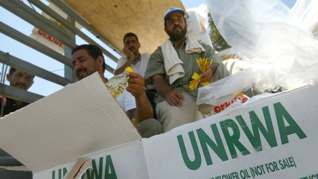 Men sit behind a box of UNRWA sunflower oil