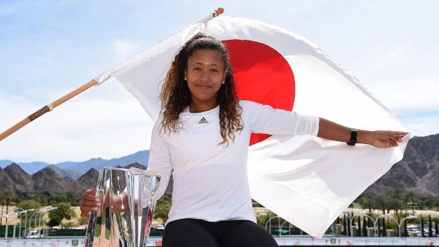 Naomi Osaka poses with the championship trophy in front of a Japanese flag on March 18, 2018 in Indian Wells, California.