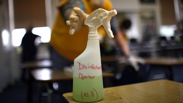 Person reaches for bottle of disinfectant spray to clean a school classroom