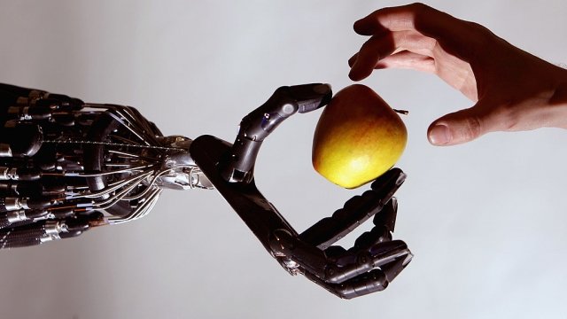 A robot made by the Shadow Robot company hands a person an apple at a robotics event in London, England