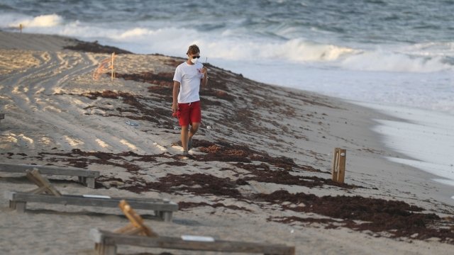 A Lake Worth lifeguard wears a protective mask and walks on a deserted beach