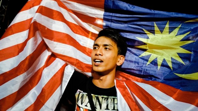 A man holding up a Malaysian flag over his shoulders