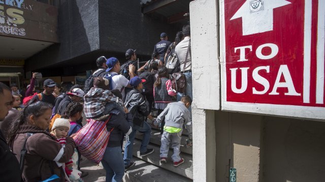 Members of the migrant caravan walking next to a sign wit "To USA' written on it