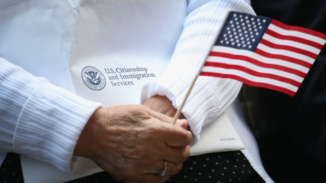 A new citizen holds a USCIS envelope and an American flag