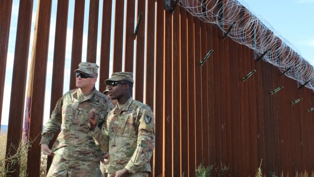 Two soldiers walk along the southern border wall.