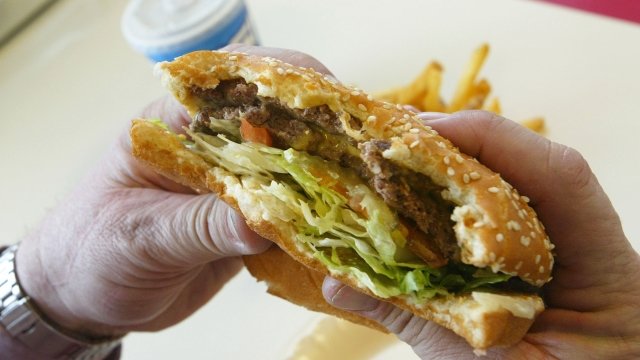 A person eats a cheeseburger with a soda
