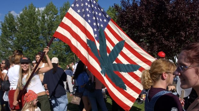 A woman holds an American flag with a marijuana leaf on it