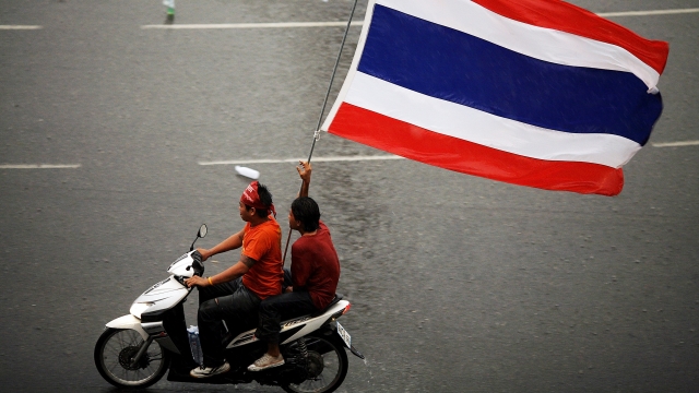 Protesters ride a motorcycle down a street in Thailand
