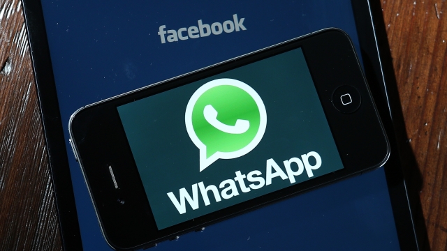 A smart phone with the WhatsApp logo sits atop a tablet displaying the Facebook logo