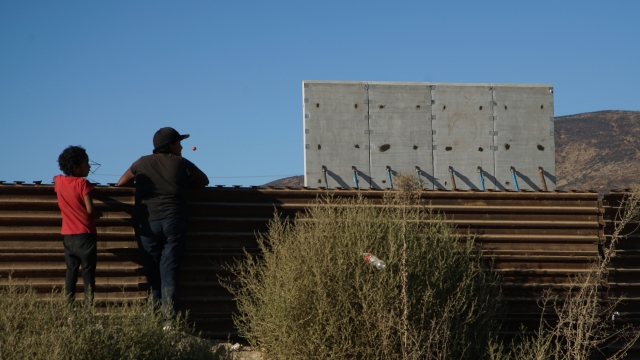 People look over the U.S. - Mexico border at President Trump's new border wall prototypes