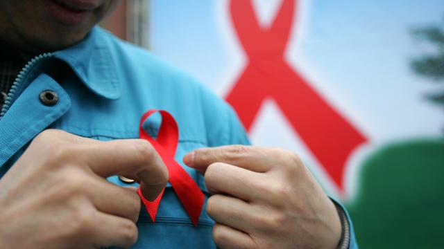 A person wears a red HIV/AIDS awareness ribbon