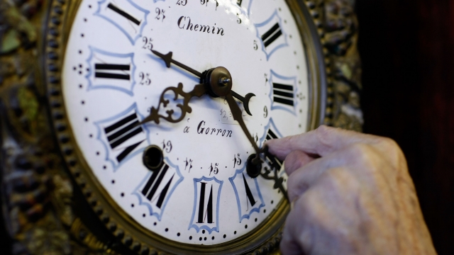A person moves a clock forward for Daylight Saving Time