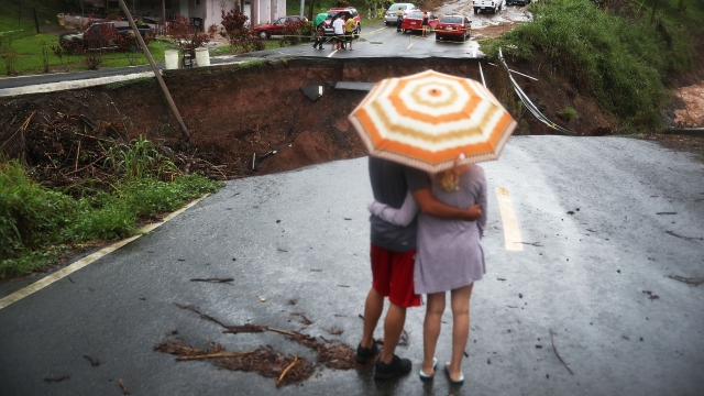 People look on at a section of a road that collapsed after a hurricane