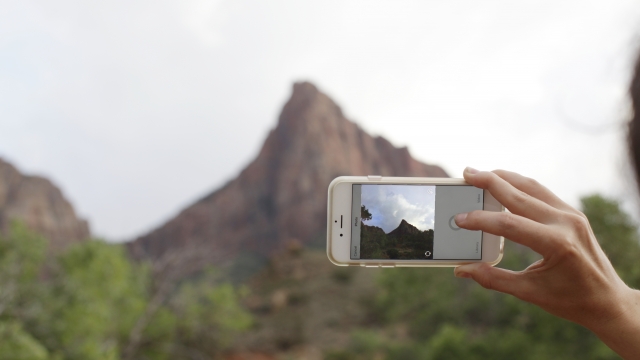 A woman takes a photo for Instagram of a ridge at Zion National Park in Utah