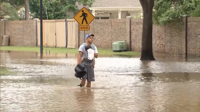 Man carries baby through flooded street.