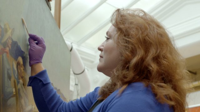 Conservator rubbing a painting with a swab
