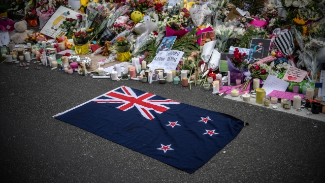 A New Zealand flag is placed next to flowers and tributes