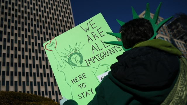 An activists holds a sign that reads, "We are all immigrants. Here to stay."