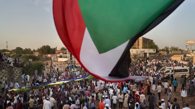 The flag of Sudan waves over a crowd of protesters.