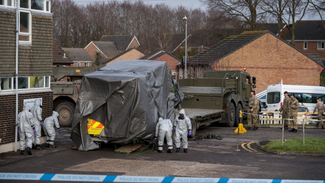 Military personnel wearing protective suits load an ambulance on to a truck as they prepare to remove it\