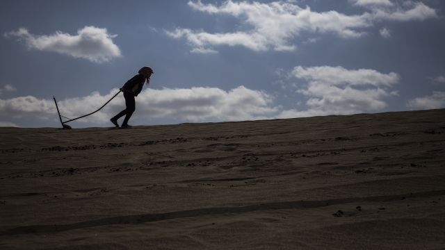 A person drags a plough through sand