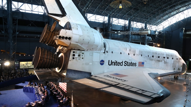 Panel sits on stage in front of a United States space shuttle