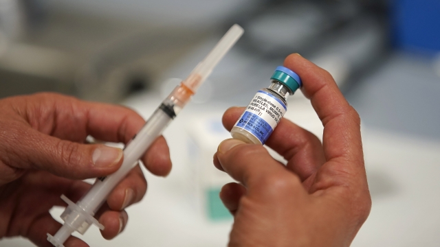 A person holds up a needle and a vial of the measles-mumps-rubella vaccine