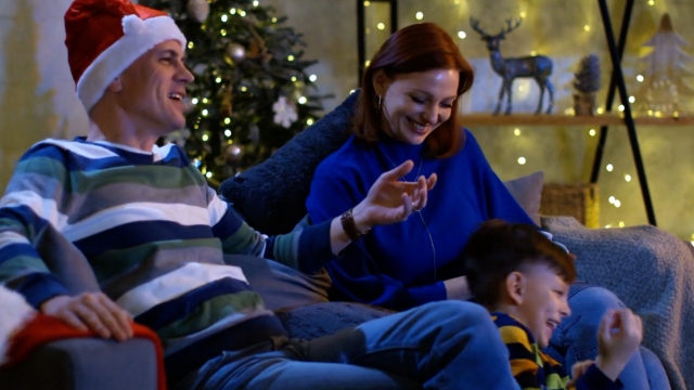 Family watches movies surrounded by Christmas decorations.