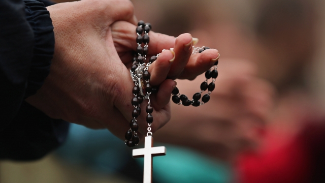 A woman holds rosary beads while she prays.