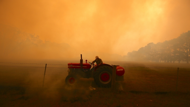 A farmer in Australia drives a tractor as he uses a hose to put out a fire