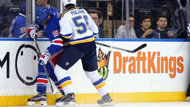 The New York Rangers and St. Louis Blues skate in front of a dasher board advertising the betting website DraftKings