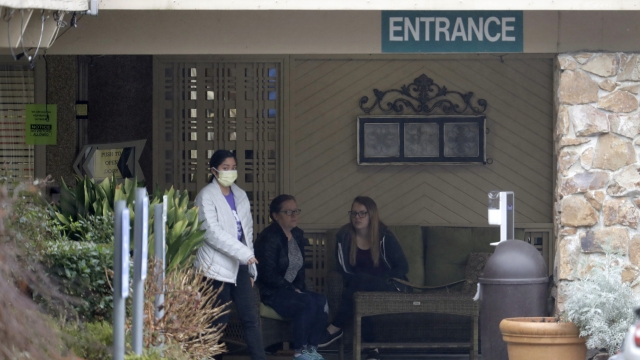 A person wearing a mask walks past a sign banning visitors at the Life Care Center in Kirkland, Wash.