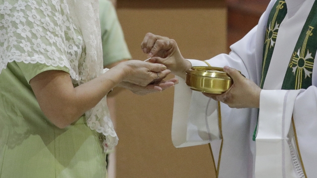 A priest places the host on the hands of a woman during a mass.