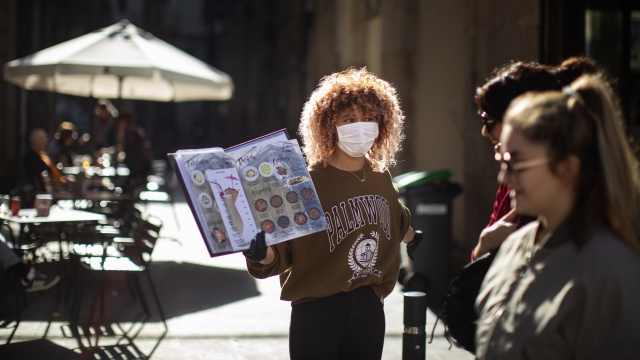 A waiter shows a restaurant menu to pedestrians in downtown Barcelona, Spain, Friday, March 13, 2020