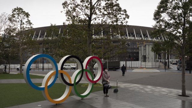 A woman pauses for photos next to the Olympic rings near the New National Stadium in Tokyo