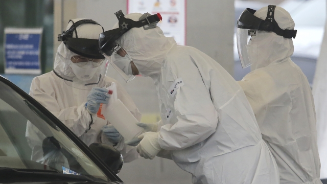 Medical staff wearing protective suits take samples from a driver with suspected symptoms of the coronavirus